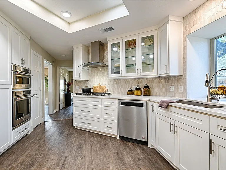 Traditional white kitchen remodel in Carrollton TX with glass-front cabinets and skylight by UHS Remodeling