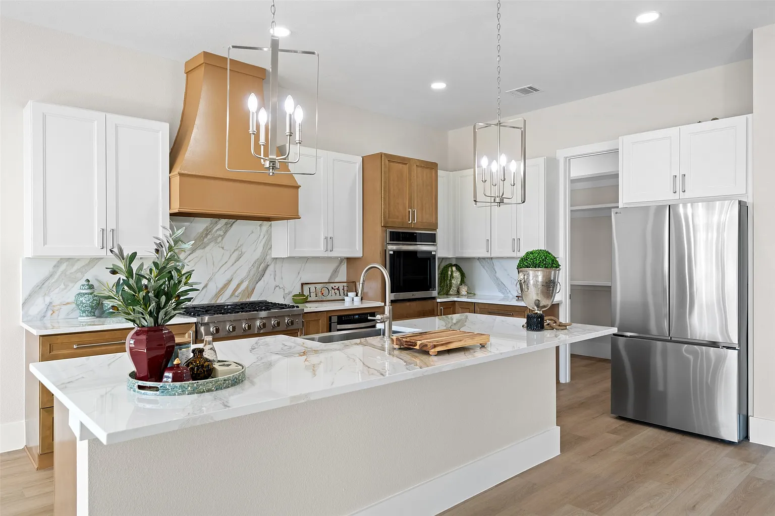 Styled kitchen with custom wood hood and marble waterfall island in builder kitchen upgrade Frisco TX by UHS Remodeling