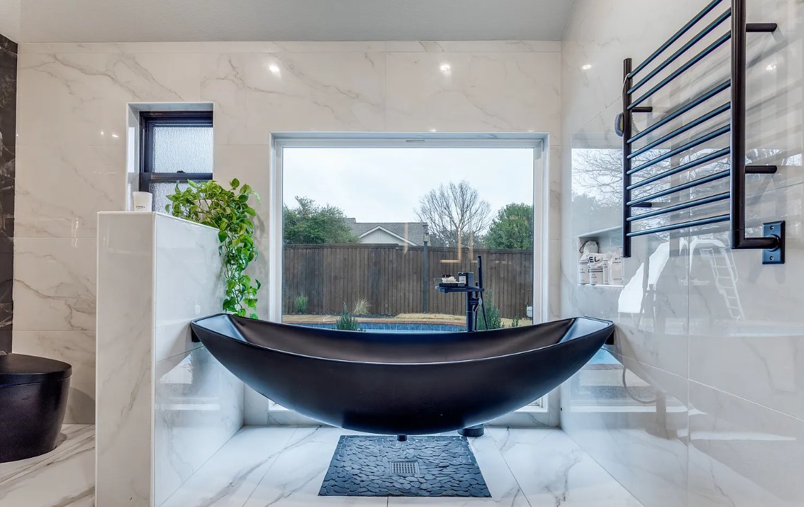 Black freestanding soaking tub with garden window view in luxury bathroom remodel Plano TX by UHS Remodeling