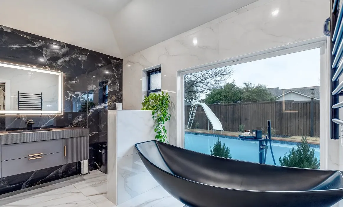 Black freestanding soaking tub with backyard pool view in a Plano, TX luxury bathroom remodel by UHS Remodeling
