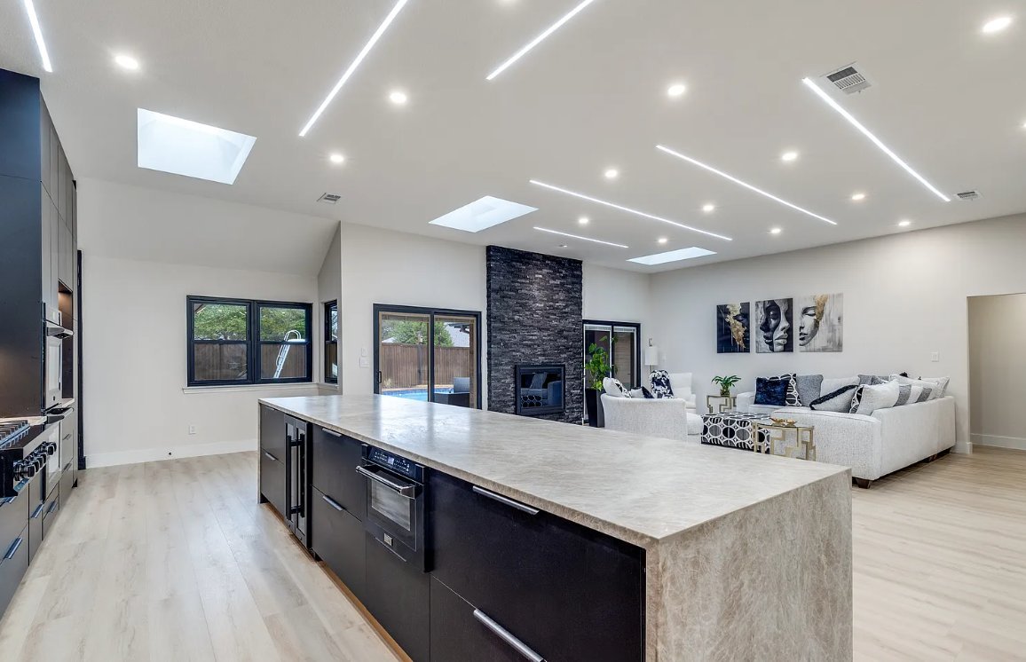 Open plan modern kitchen facing stone fireplace living room in Plano TX by UHS Remodeling