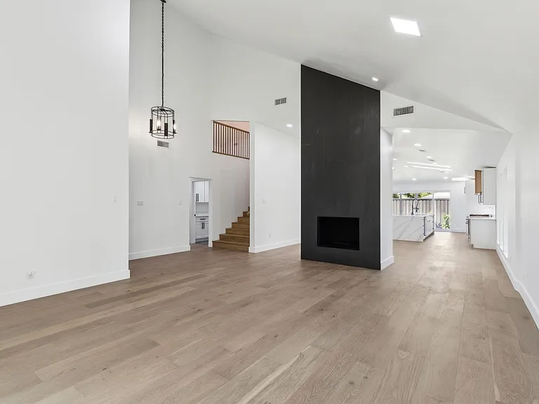 Open great room with black fireplace wall and wide plank floors after 1970s home renovation Richardson TX by UHS Remodeling
