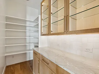 Butler pantry with glass-front lit cabinets and marble counter in The Colony TX by UHS Remodeling