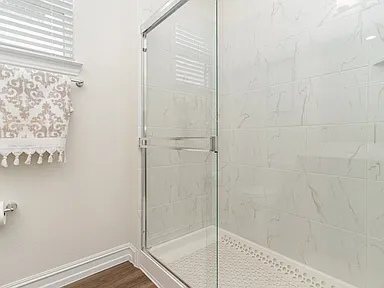 Walk-in shower with marble tile and frameless glass in Wylie TX bathroom by UHS Remodeling