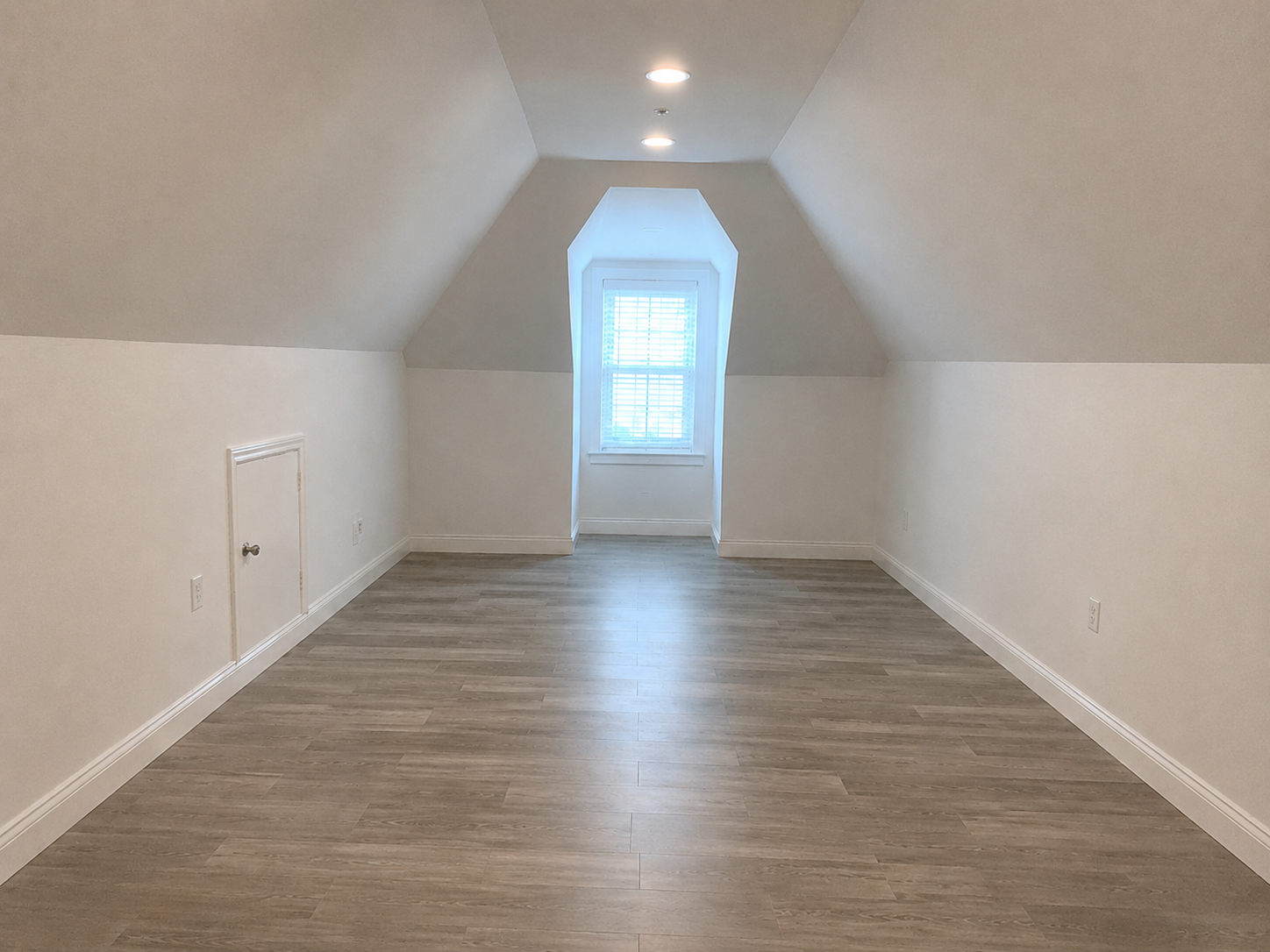 Converted attic bedroom with a sloped ceiling, dormer window, and wood-look floor by UHS Remodeling in Dallas-Fort Worth