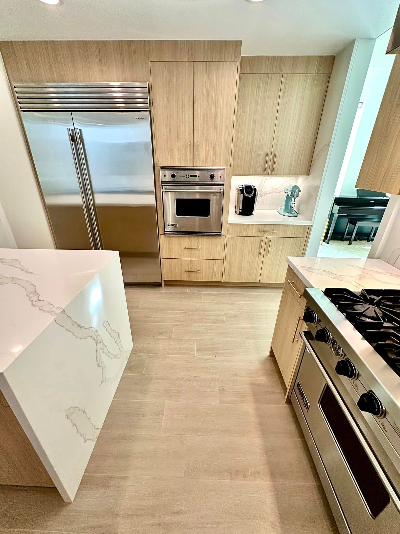 Luxury kitchen interior remodel with light wood cabinets and a marble waterfall island in Dallas, TX by UHS Remodeling