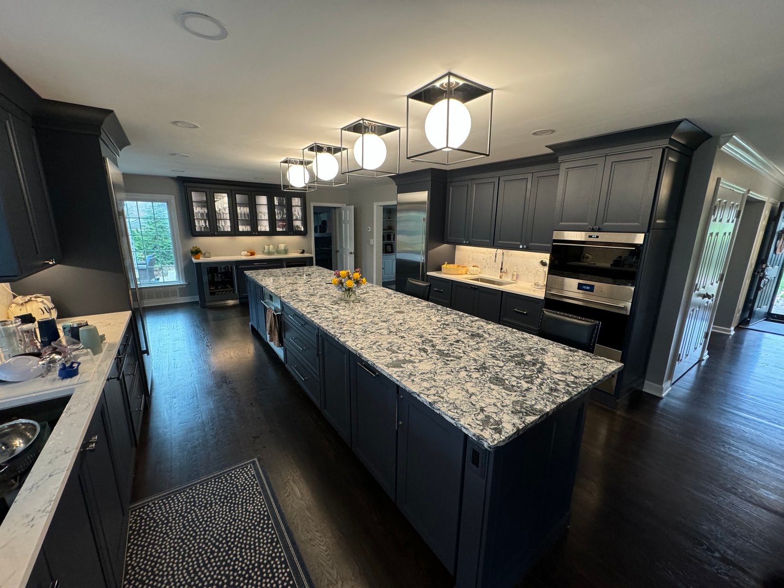 Navy kitchen with a granite waterfall island, glass-front cabinets, and lantern pendants in an Allen, TX interior remodel by UHS Remodeling